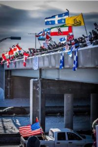 trucker protest crowd on overpass with flags